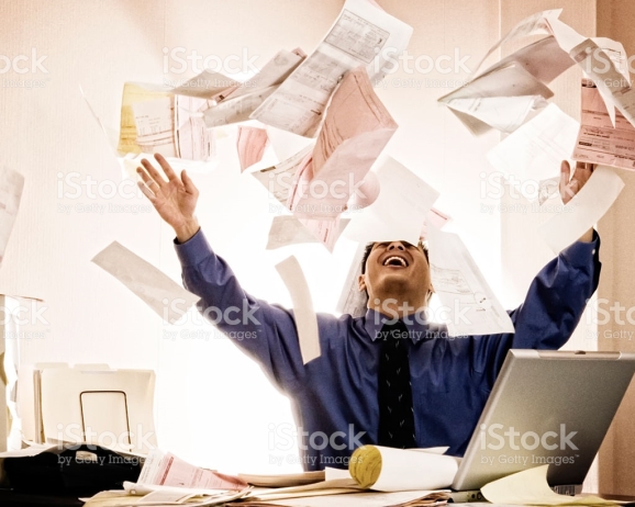Happy businessman tossing documents into air at desk.